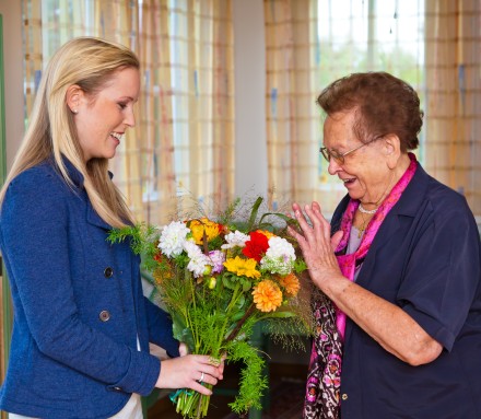 Junge Frau besucht Grossmutter mit Blumen